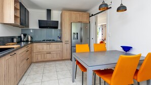 A modern kitchen with wooden cabinets, a stainless steel refrigerator, and a dining area with orange chairs. - Holiday Home 'Maison Ker Hélène' with Private Terrace, Wi-Fi and Air Conditioning (Guérande)