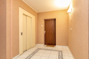 Un couloir doté d’un sol recouvert de moquette, d’une porte en bois et d’un luminaire fixé au mur.