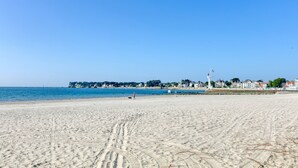Een zandstrand met een helderblauwe lucht, enkele mensen en gebouwen op de achtergrond.