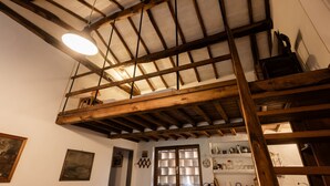 A loft-style room with exposed wooden beams, a skylight, and a loft bed.