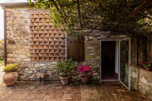 Un edificio in pietra con un muro in mattoni, persiane di legno e piante in vaso.