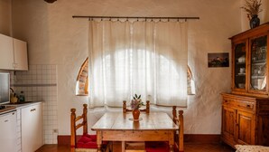 A kitchen with a dining table, chairs, a cabinet, and a window with curtains.