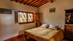 A bedroom with a wooden ceiling, a bed with a floral bedspread, a window with a lattice design, and a bookshelf.