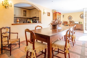 A dining area with a wooden table and chairs, a kitchen in the background, and a decorative plant centerpiece.