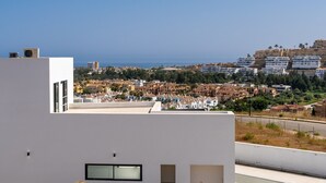 Un edificio moderno con techo plano, grandes ventanales y vistas a un pueblo costero con edificios y vegetación.