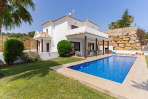 A modern villa with a swimming pool, a patio with outdoor furniture, and a stone wall.