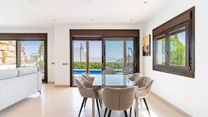 Comedor moderno con una mesa de vidrio, cuatro sillas y vista a una piscina.
