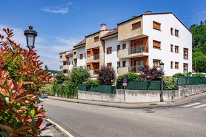A multi-story residential building with balconies, a street in front, and a pedestrian crossing.