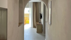 Un pasillo con suelo de baldosas, un arco de entrada y una pequeña mesa con un televisor.