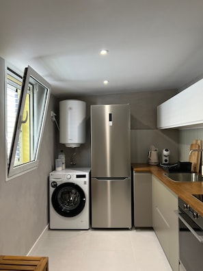 A compact kitchen with a washing machine, a stainless steel refrigerator, and a built-in oven.
