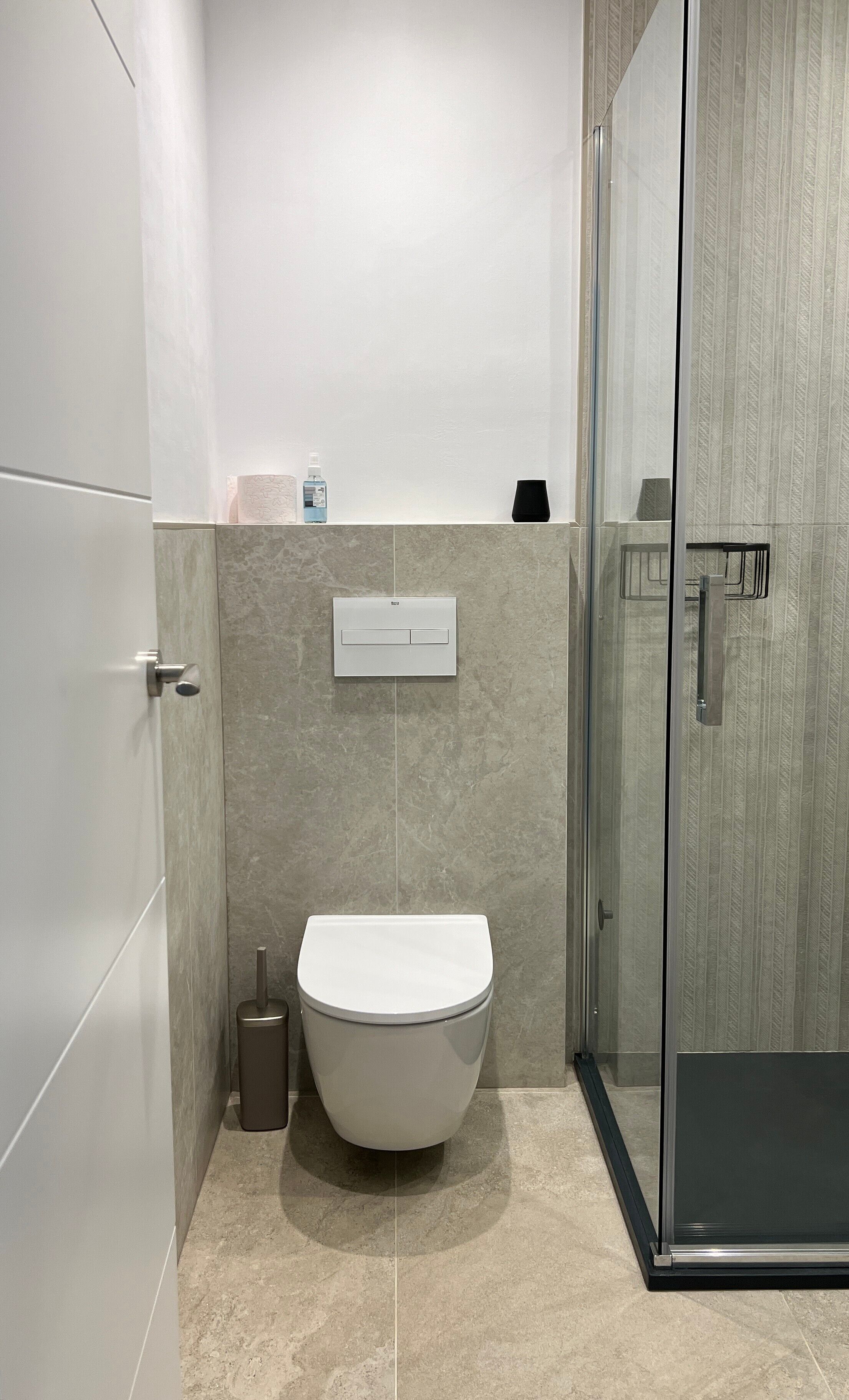 A modern bathroom with a toilet, a hand dryer, and a glass shower enclosure.