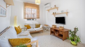 Un salon avec un canapé, un téléviseur, des étagères en bois et une plante en pot.