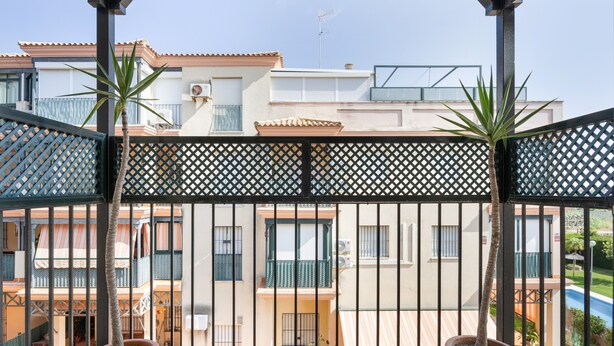 Un balcon orné de plantes en pot, une vue sur un immeuble d’habitation et un ciel dégagé.