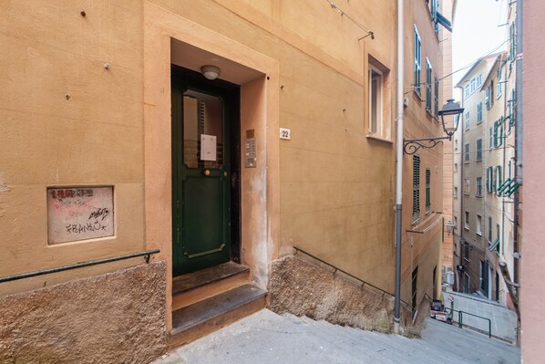 A narrow street with a building entrance, a green door, and a small sign with numbers.