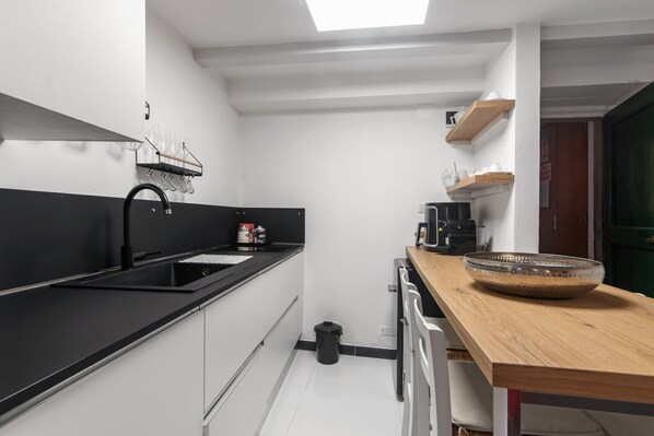 A modern kitchen with a black countertop, white cabinets, a black sink, and a wooden table with a bowl.