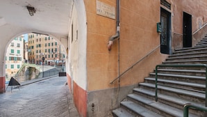 Una escalera conduce a un piso superior, un letrero que dice 'SALITA DEL PRIARO' y una vista de la calle con edificios al fondo.