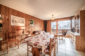 A wooden room with a dining table, chairs, a sofa, a window with a view, and a lamp. - Edelweiss Apartment for 7 with Mountain View, Shared Garden, and Balcony (Morillon)