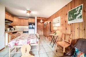 A wooden interior with a dining table, chairs, a small table with a bottle, and a poster on the wall. - Apartment 'Edelweiss - 7 Personnes' with Mountain View, Shared Garden and Balcony (Morillon)
