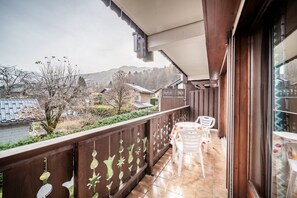 A balcony with a wooden railing, a table with chairs, and a view of houses and trees. - Edelweiss Apartment for 7 with Mountain View, Shared Garden, and Balcony (Morillon)