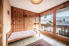 A wooden room with a bed, a large window, and a view of mountains. - Edelweiss Apartment for 7 with Mountain View, Shared Garden, and Balcony (Morillon)
