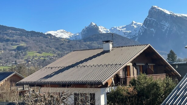 Una cabaña con techo inclinado, fachada de madera y vistas a montañas nevadas.