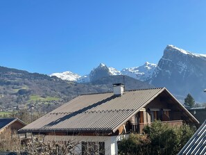 A chalet with a sloped roof, wooden exterior, and a view of snow-capped mountains. - Apartment 'Edelweiss - 7 Personnes' with Mountain View, Shared Garden and Balcony (Morillon)