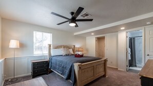 A bedroom with a bed, bedside tables, a ceiling fan, a window, and an open door leading to a bathroom.