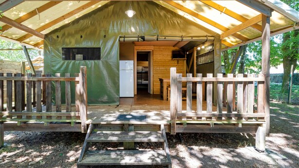 Eine Holzhütte mit verdeckter Veranda, einer Küchenzeile und einem kleinen Kühlschrank.