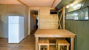Eine kleine Küche mit Kühlschrank, Holztisch und Bank sowie einem an der Wand befestigten Fernseher.