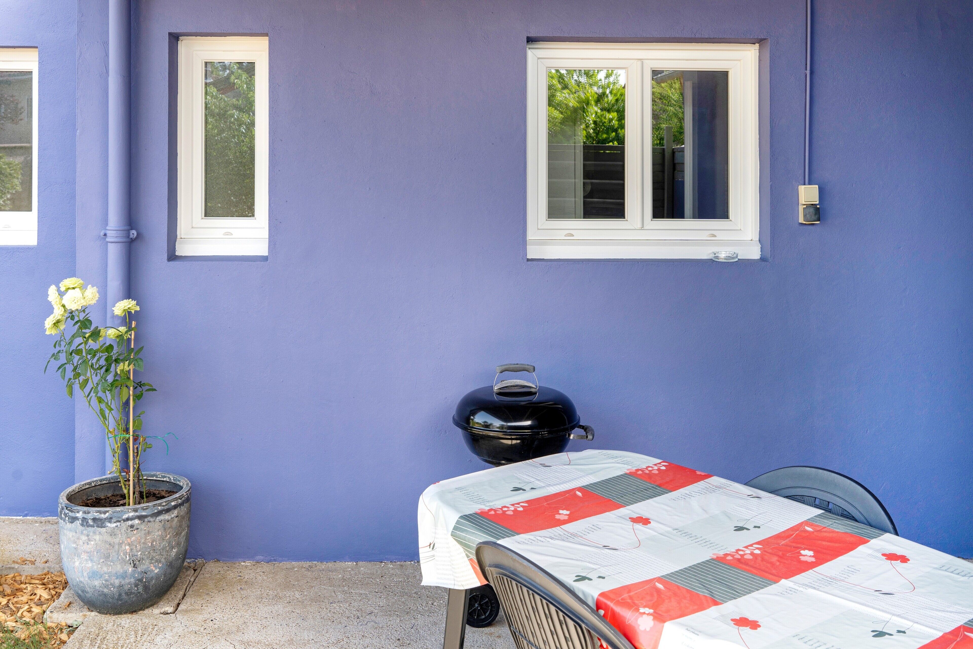A patio with a table covered by a floral tablecloth, a black grill, and a potted plant.