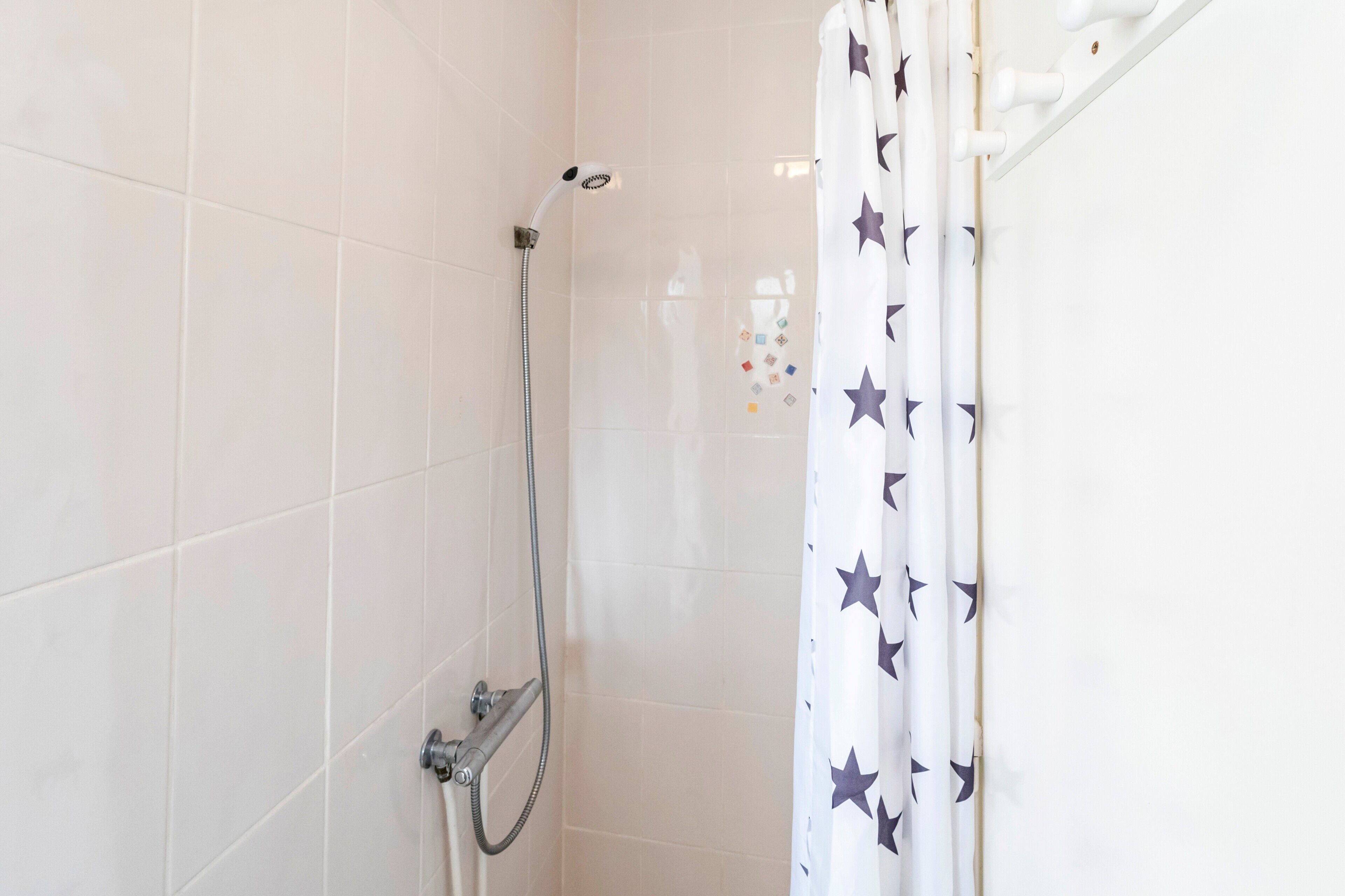 A shower with a handheld showerhead, a wall-mounted faucet, and a shower curtain with a star pattern.