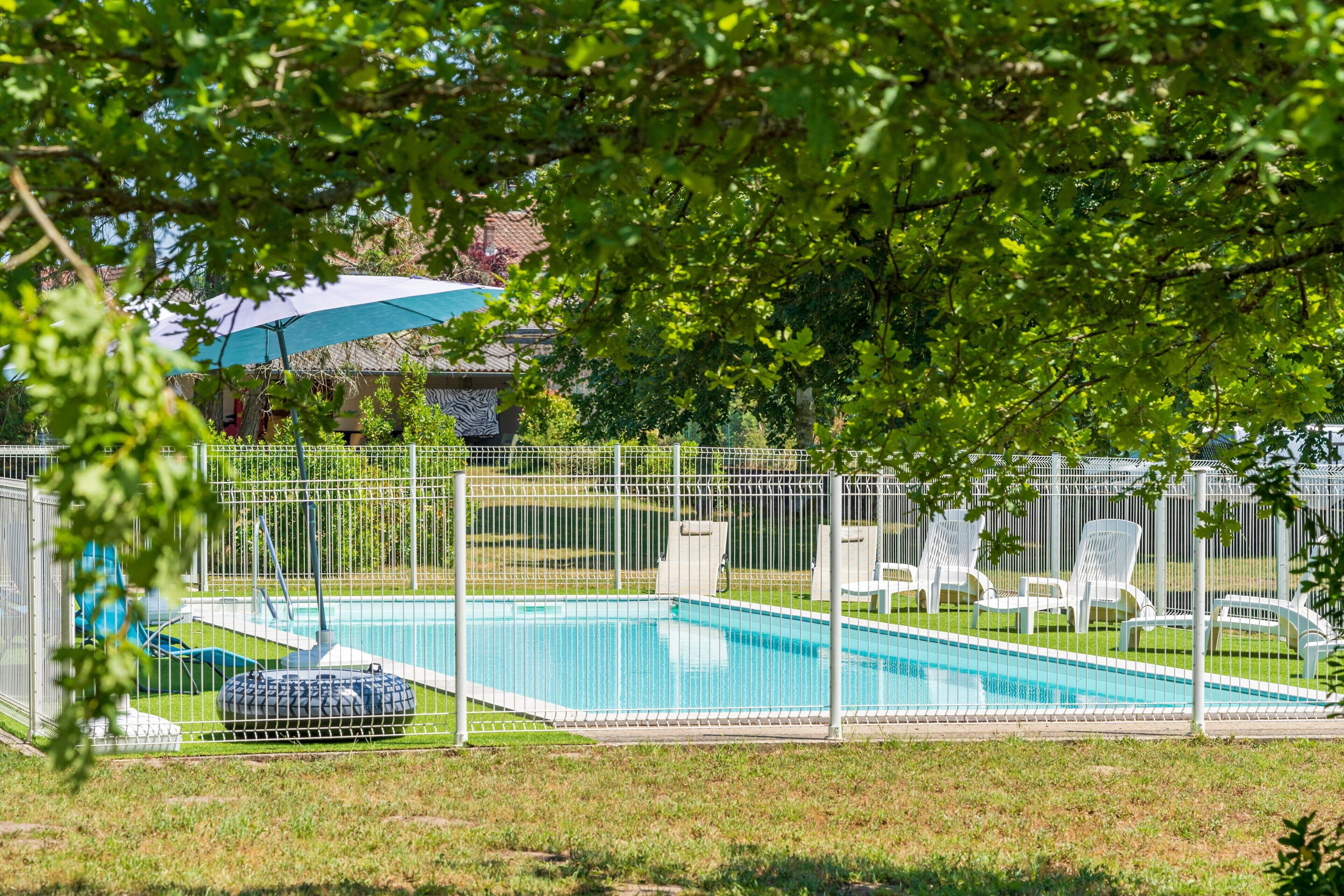 A swimming pool with a fenced area, lounge chairs, and a covered seating area.