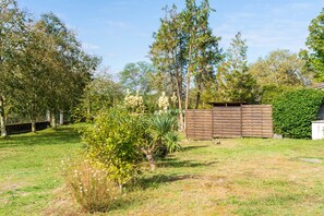 A grassy yard with a wooden fence, trees, and a small bush.