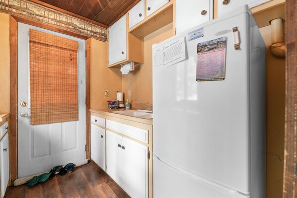 A compact kitchen with white cabinets, a refrigerator, a sink, and a wooden floor.