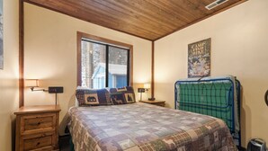 Een slaapkamer met een bed, twee nachtkastjes, een raam, een poster aan de muur en een koffer.
