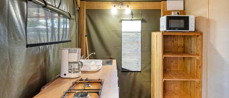 A compact kitchen with a gas stove, coffee maker, and a microwave on a shelf.