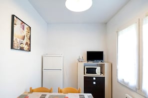 A small room with a table, chairs, a refrigerator, a microwave, a television on a cabinet, and a window with curtains. - "Bruyères - Domaine Des Landes" with shared pool, private terrace, and shared garden (Lesperon)