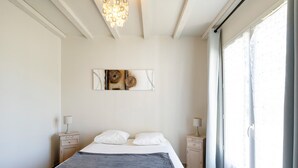 Une chambre à coucher comprenant un lit, des tables de chevet, un lustre, une fenêtre avec des rideaux et une œuvre d’art murale.