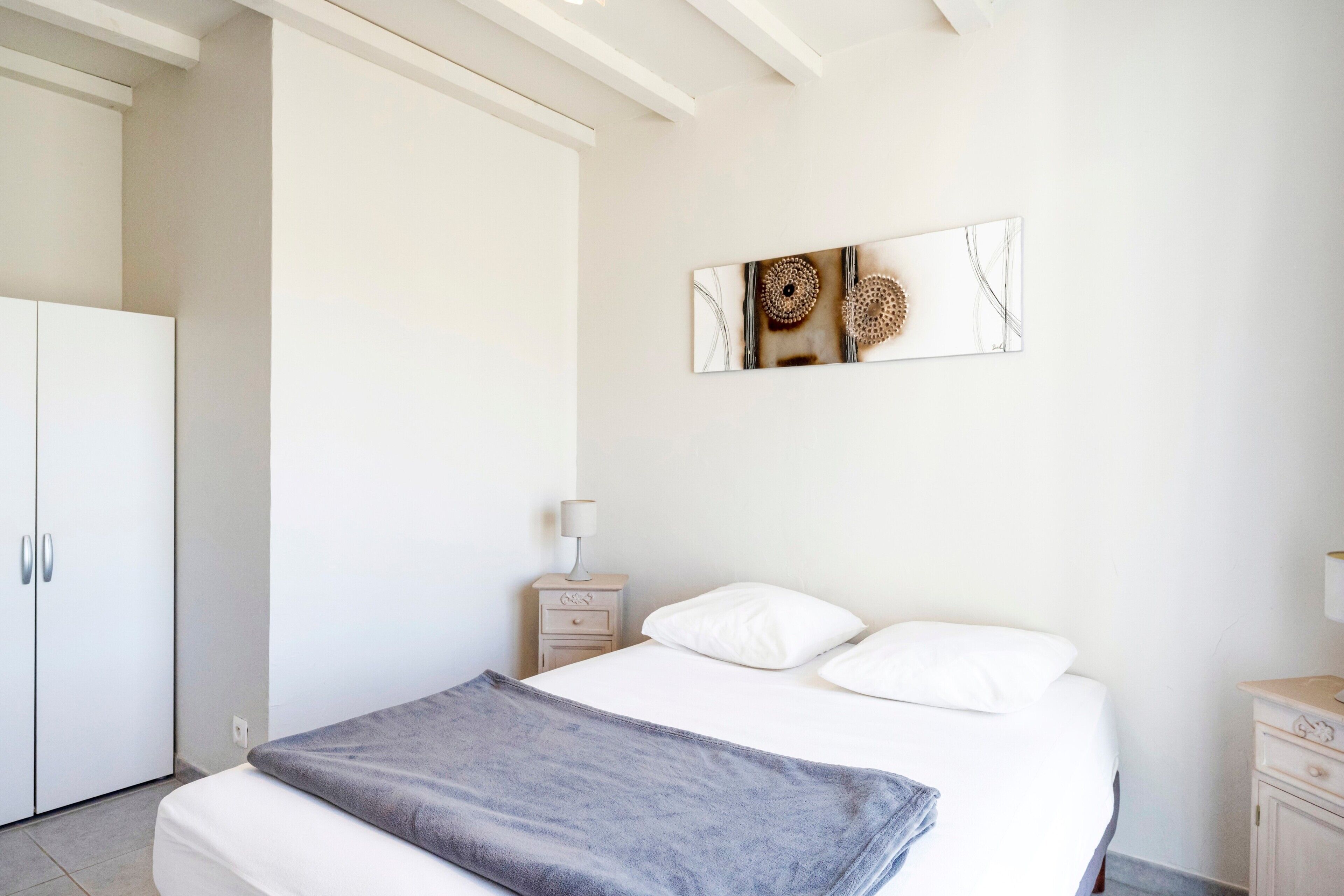 A bedroom with a bed, a nightstand, a lamp, a wardrobe, and a wall art piece.