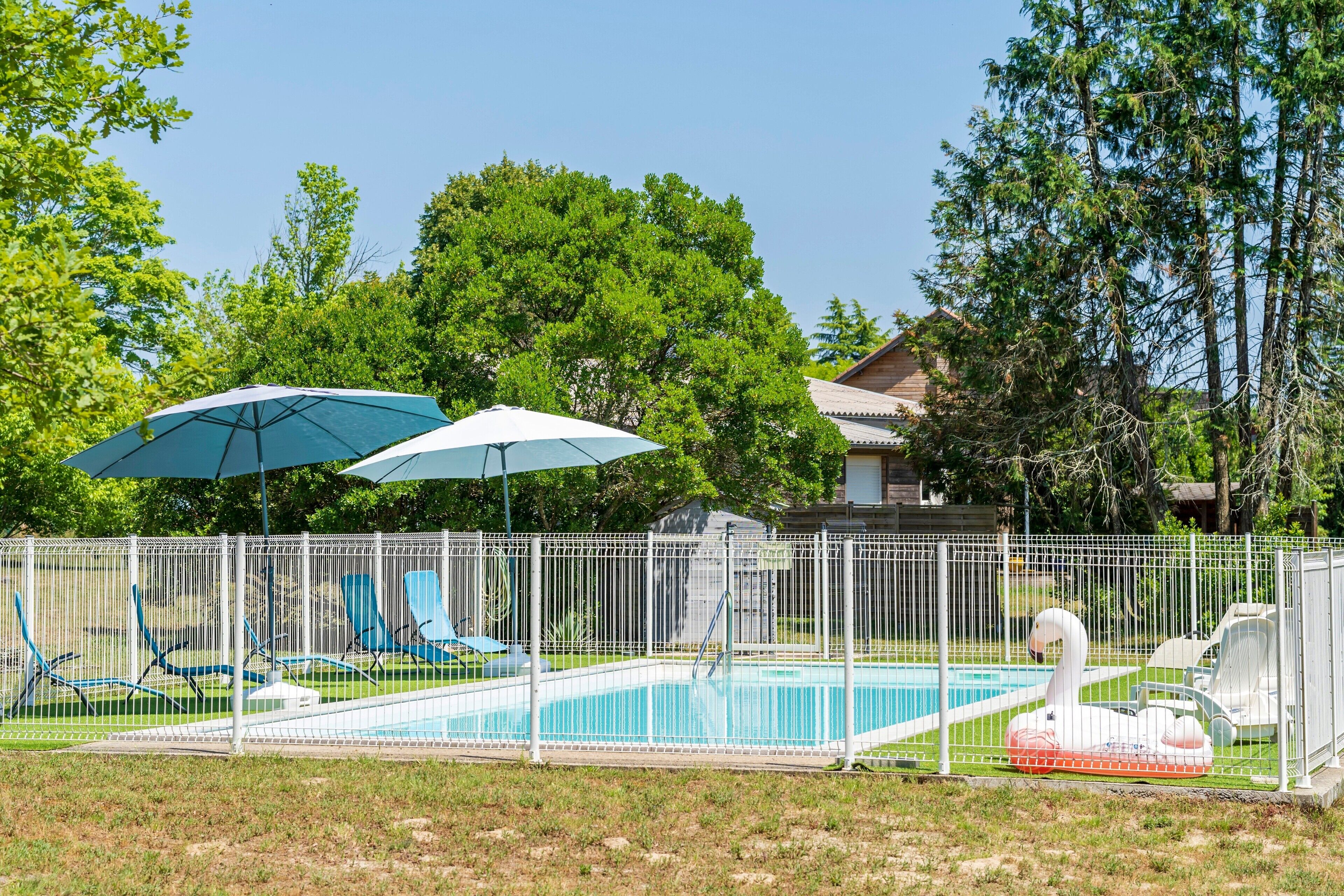 Una piscina con sillas de descanso y sombrillas, rodeada por una cerca blanca.