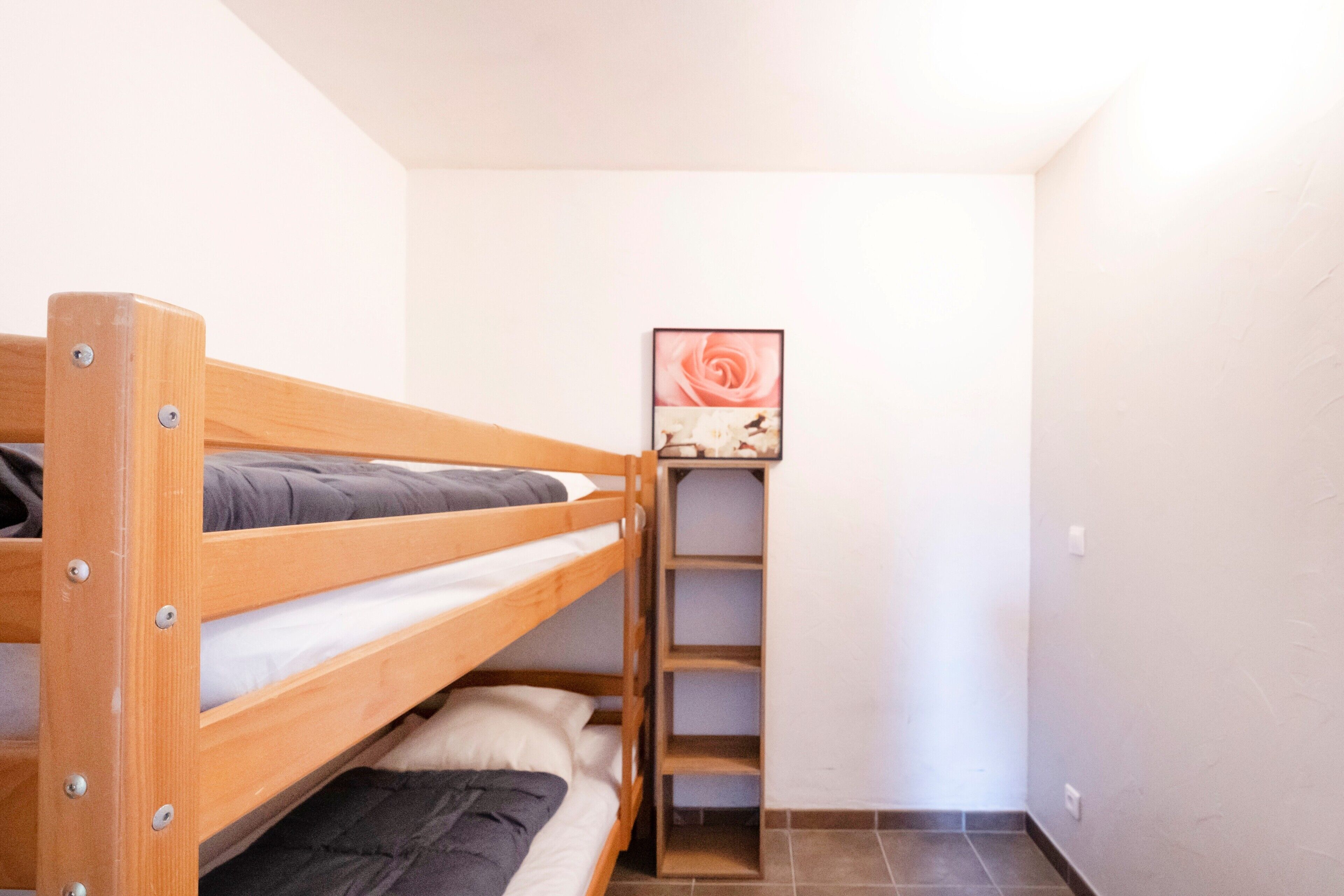 Un lit superposé avec une structure en bois, une petite étagère et un tableau encadré accroché au mur.