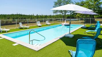 Une piscine entourée d’une clôture blanche, avec de l’herbe artificielle verte et plusieurs chaises longues.