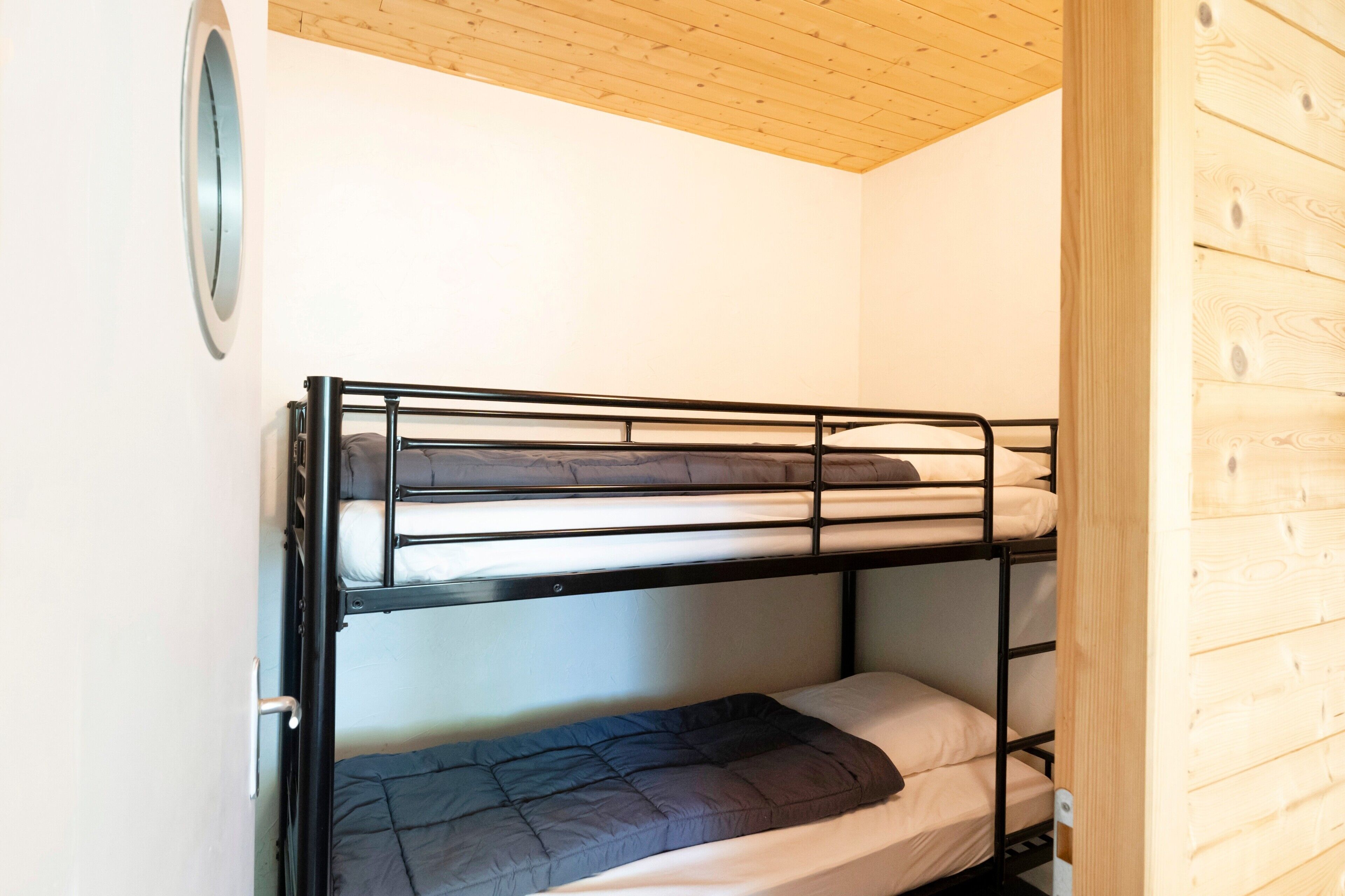 Een slaapkamer met een stapelbed, houten plafond en een witte muur.