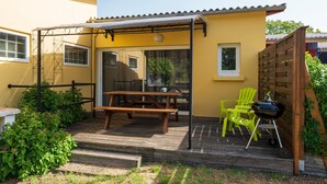 Eine Terrasse mit Holztisch und -stühlen, einem Grill und einem überdachten Bereich mit einer Pergola.