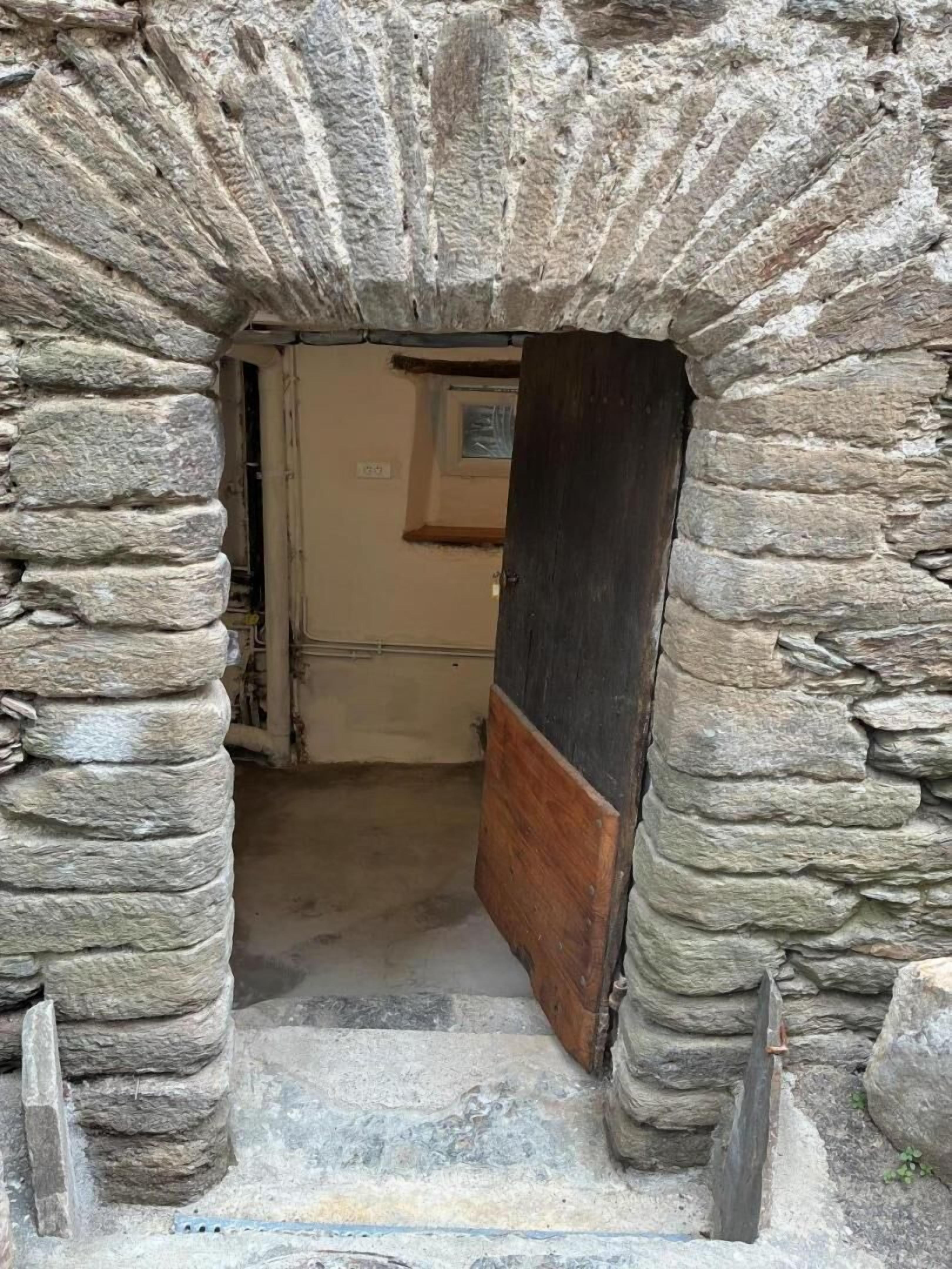 A stone archway leading to a room with a wooden door and a small window.