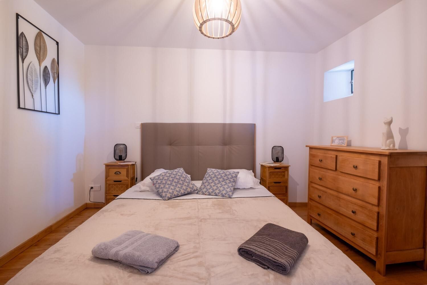 A bedroom with a large bed, two bedside tables, a wooden dresser, and a ceiling light fixture.