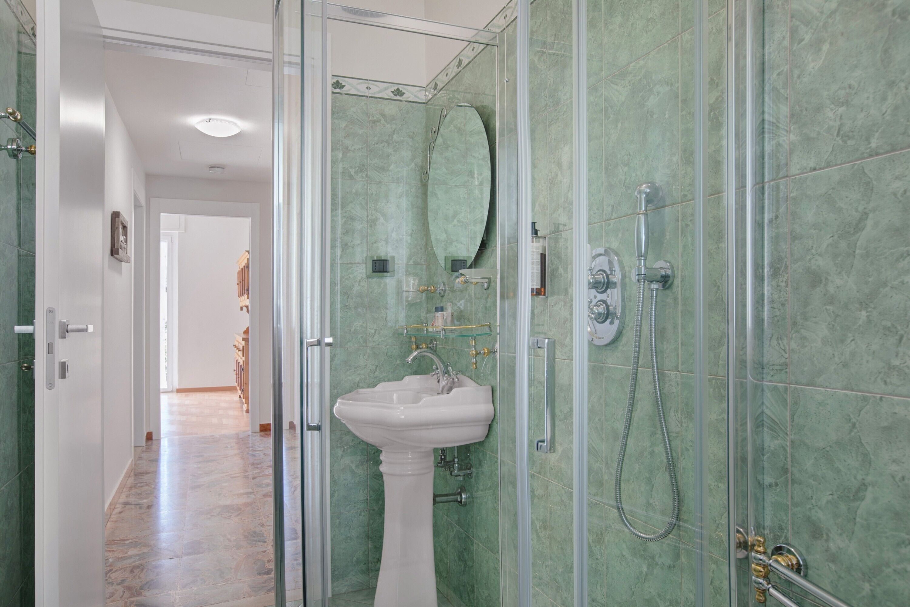 Une salle de bain avec une douche à parois de verre, un lavabo sur colonne et un miroir.