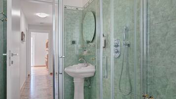 Une salle de bain avec une douche à parois de verre, un lavabo sur colonne et un miroir.