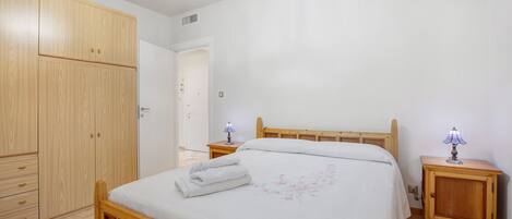 Un dormitorio con cama de madera, mesitas de noche, armario y lámpara de techo.