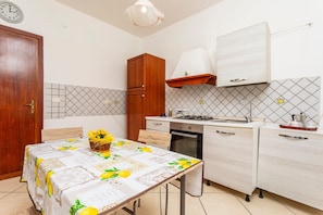 A kitchen with a dining table, wooden cabinets, a clock, and a tiled backsplash. - Apartment 'Da Lorenzo  Alcantara' with Mountain View and Wi-Fi (Gaggi)